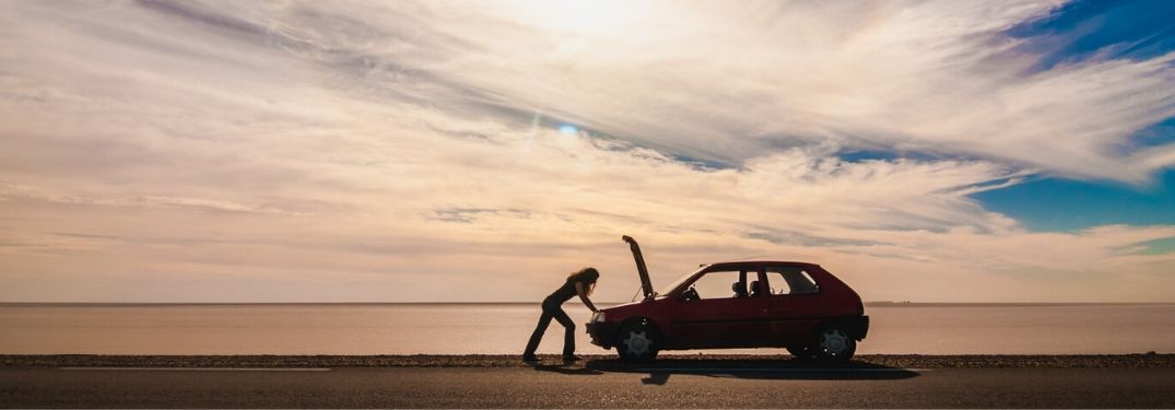 Person looking under the hood of a car in distance