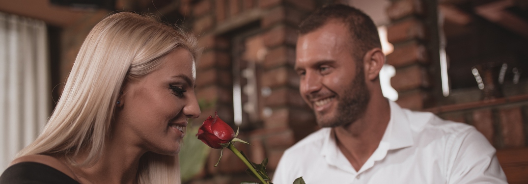 A smiling man proffers a rose up to the nose of a woman sitting near him. A mating ritual of the human species.