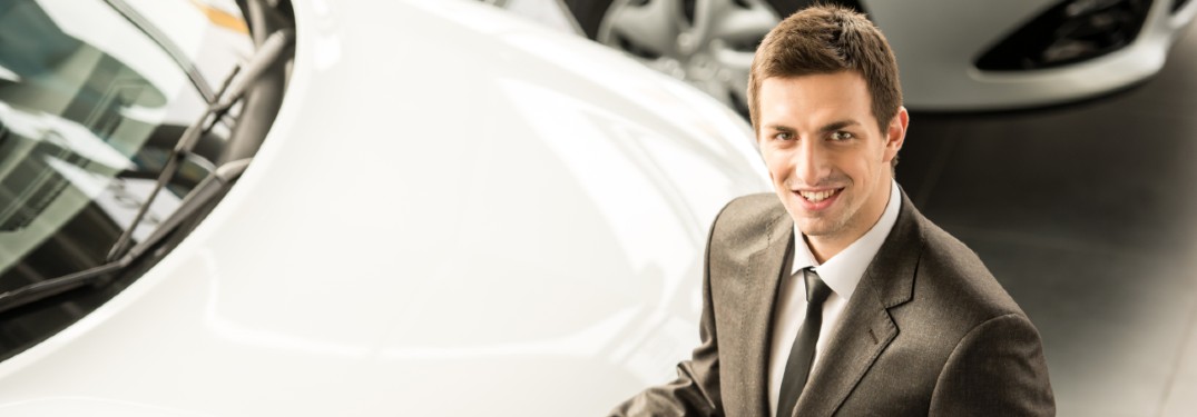 salesperson smiling up next to white car
