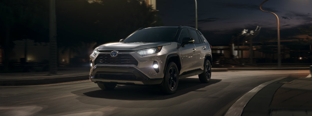 Silver 2019 Toyota RAV4 driving at night time on lit city street