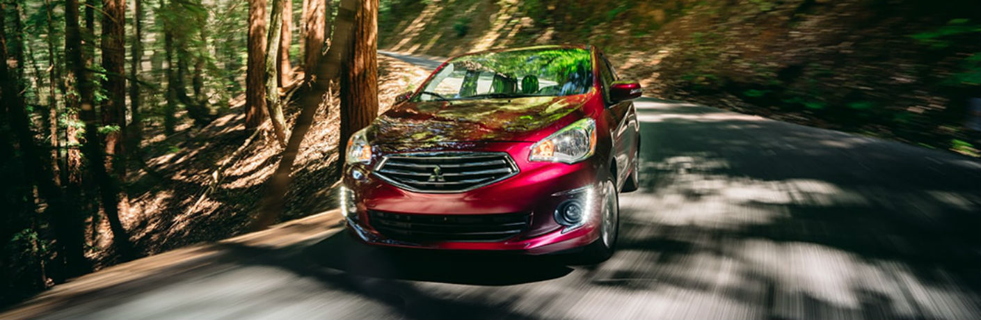 Exterior view of a red 2018 Mitsubishi Mirage G4 driving down a country road surrounded by trees