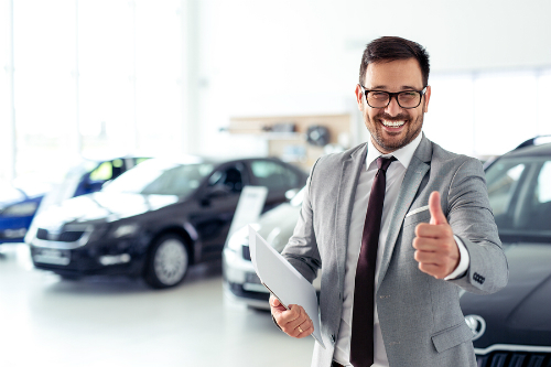 A salesman in a dealership gives an enthusiastic "thumbs up."
