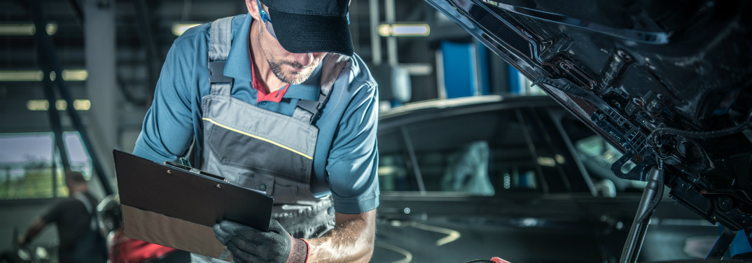 Mechanic wearing blue looks under the hood of a car