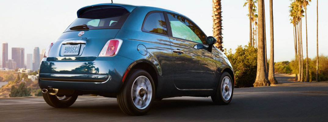 Rear view of blue 2018 Fiat 500 driving with city skyline in background