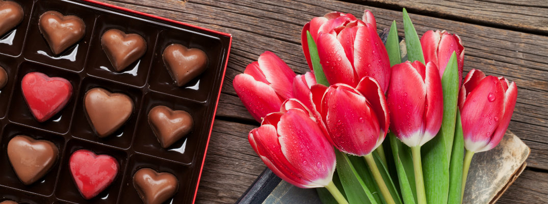a bouqet of red tulips next to a box of heart shaped chocolates