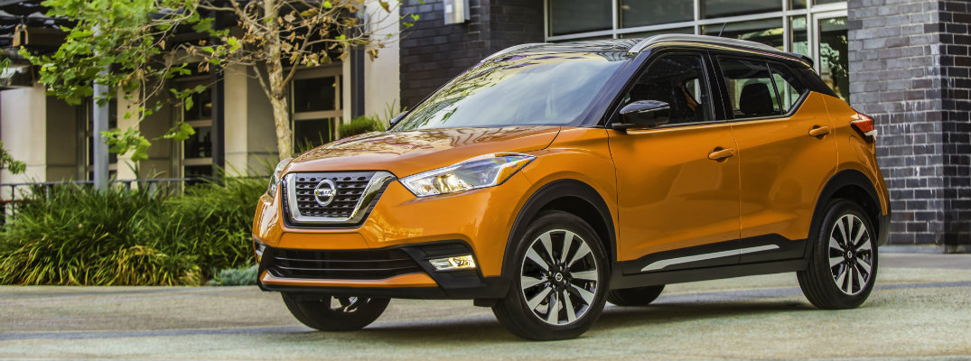 2018 Nissan Kicks orange exterior parked in the driveway of a fancy house next to a lush green yard and tree