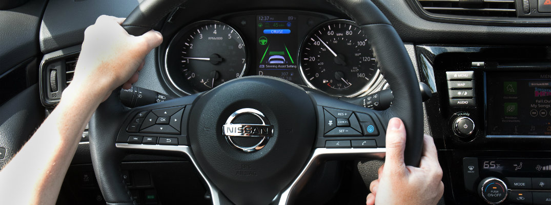 close up of driver's hand on a Nissan branded steering wheel with a digital driver's display behind the wheel