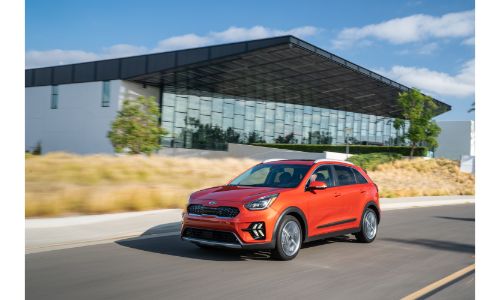 2020 Kia Niro Touring exterior shot with red paint color driving by a glass building near yellow grass