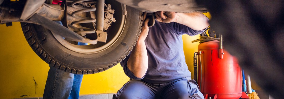 an auto mechanic in a blue jumpsuit fixing a tire on a lifted car in an auto service shop