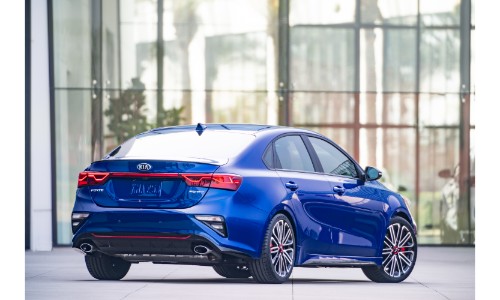2020 Kia Forte GT exterior rear shot with blue paint color parked outside the glass walls of a car dealership