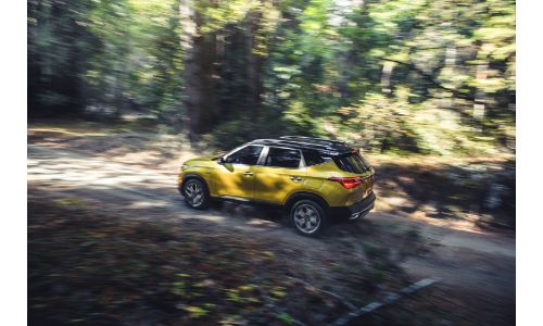 2021 Kia Seltos exterior overhead side shot with gold paint color driving through a forest under the shadow of branches
