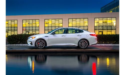 2020 Kia Optima exterior side shot with white paint color parked outside a dealreship at night