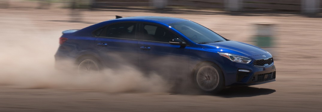 2021 Kia Forte exterior side shot with Deep Sea Blue paint color driving on a dusty dirt road and kicking up clouds