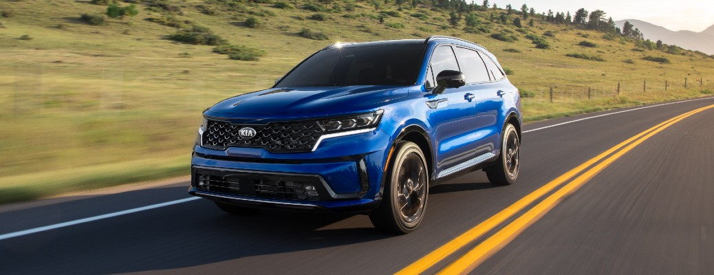 2021 Kia Sorento exterior shot with blue paint color driving down a country highway near hills of trees
