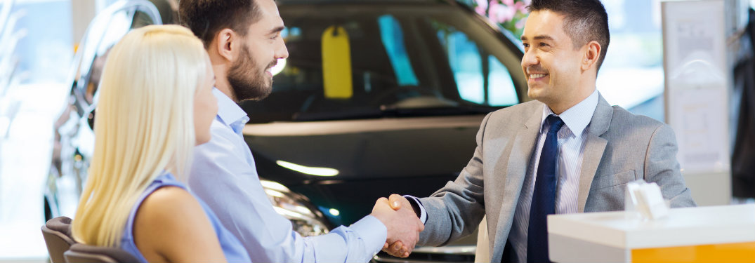 Young-couple-shaking-hands-with-salesman-at-car-dealership