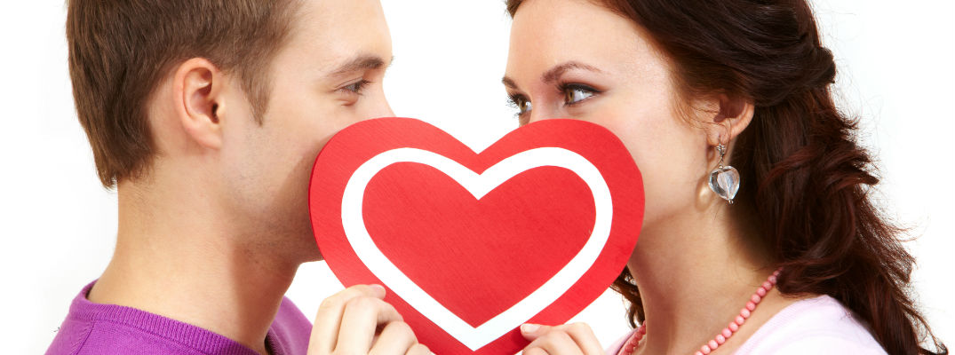 A stock photo of a young couple's faces hidden behind a paper heart