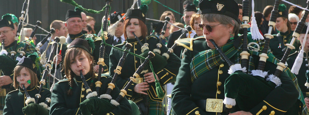 A stock photo of people marching in a St. Patrick's Day Parade carrying bagpipes