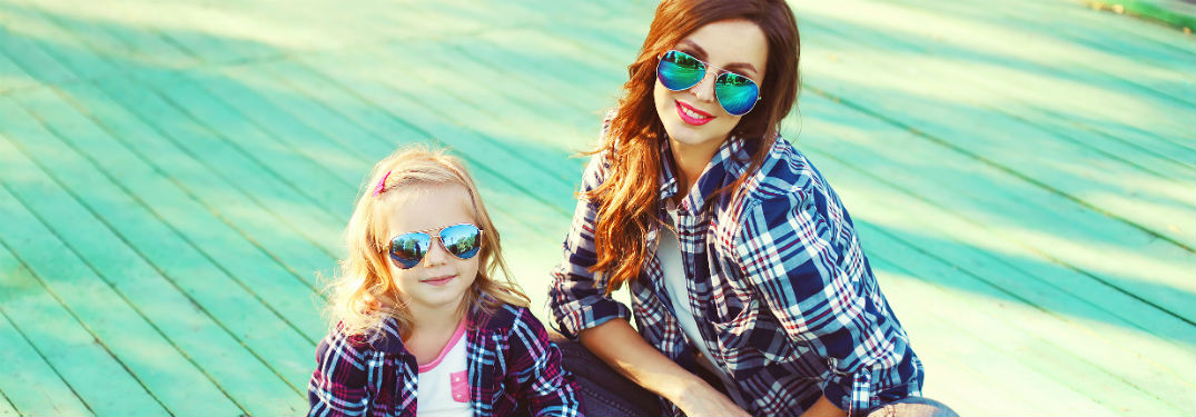 Mother and daughter in matching flannel outfits and sunglasses sitting on blue deck