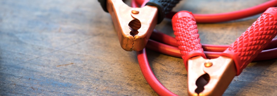 Red and black car battery jumper cable, or booster cables. Focus on black clamp tip. Shallow depth of field.