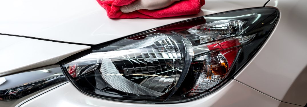A person cleaning a vehicle's headlights with a red cloth