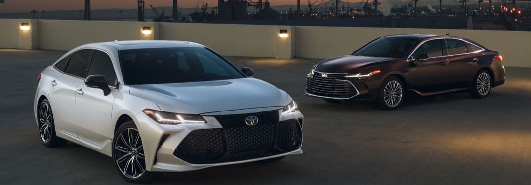 2020 Toyota Avalon Touring on left and Hybrid Limited on right with city in background