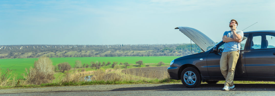 man-on-phone-leans-up-against-car-with-open-hood-on-side-of-road