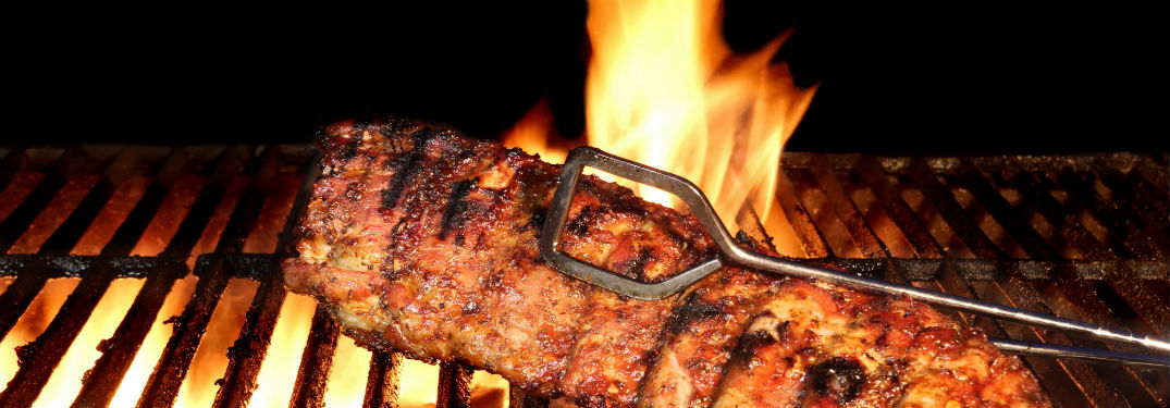 bbq roast baby back ribs on grill with fire and tongs