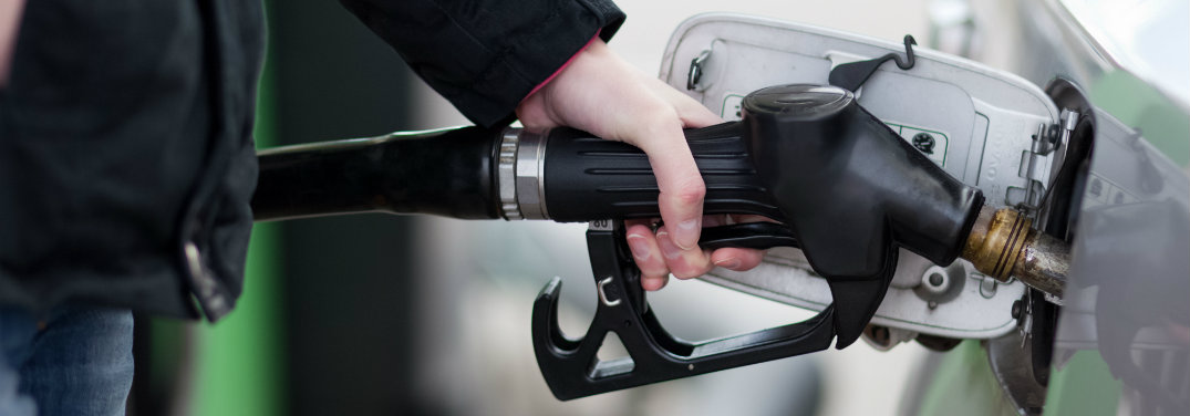 person putting black gas pump nozzle in car