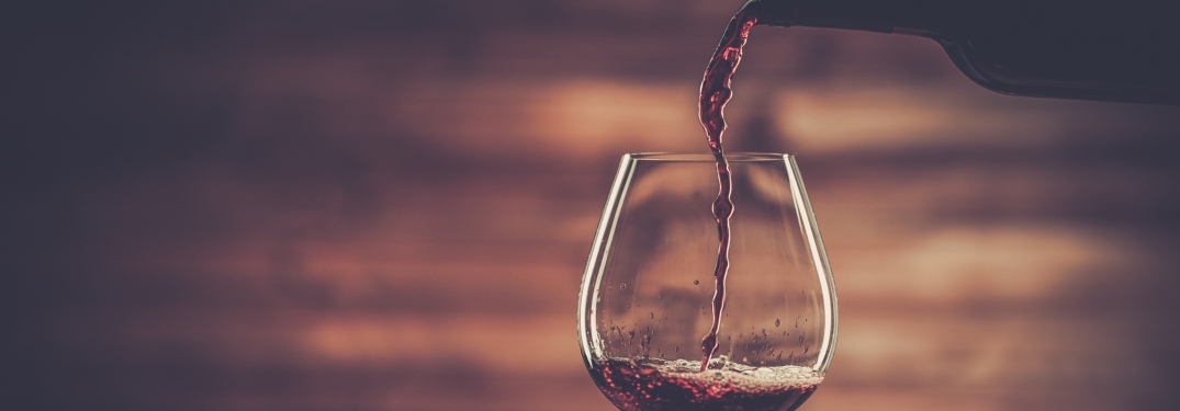 Pouring red wine into the glass against wooden background