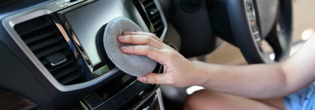 A woman cleaning a car's infotainment screen