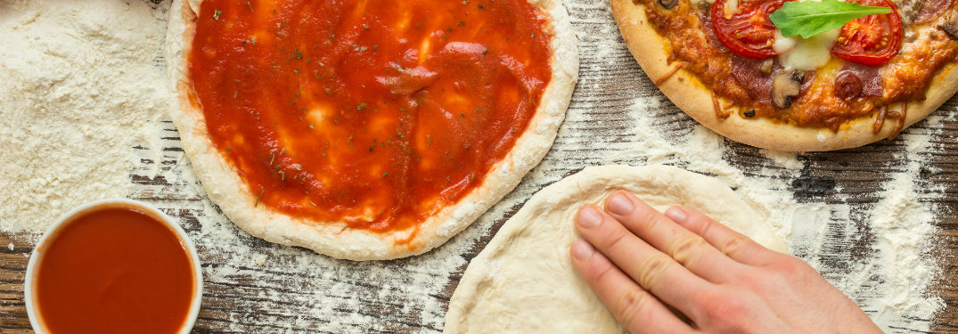 person kneading dough and making pizza with ingredients on table