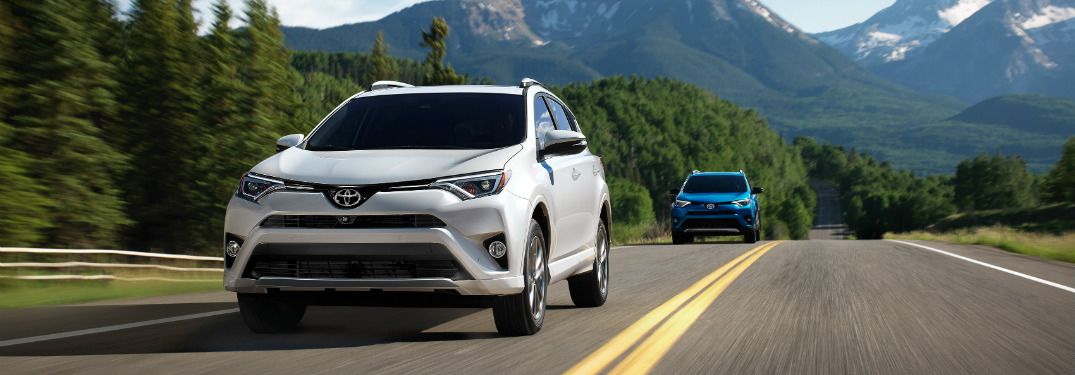 white 2018 toyota rav4 hybrid followed by blue rav4 driving on highway with mountains in background