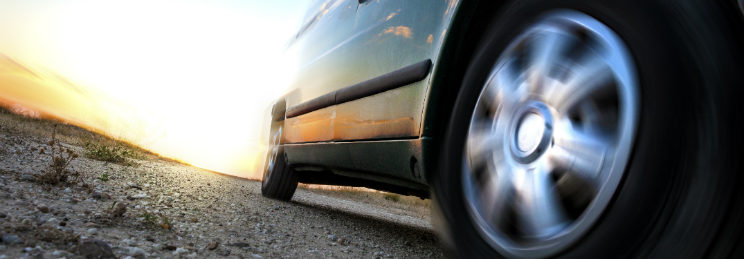 generic car tire driving on asphalt road with sun behind it