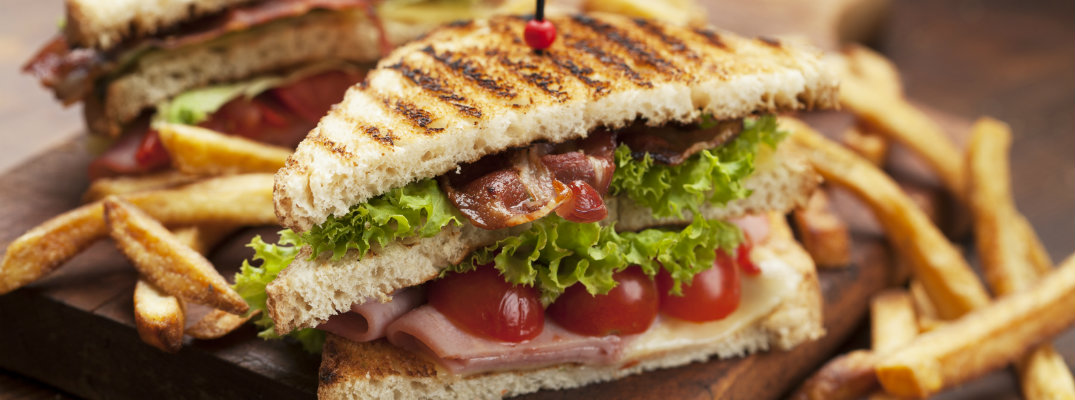 ham and bacon club sandwhich on cutting platter with fries