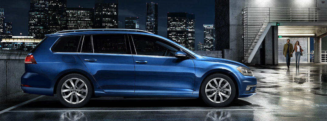 2018 Volkswagen Golf SportWagen silk blue metallic exterior shot parked on a roof at nightime with lit up skycrapers in the background as a couple walks towards their car