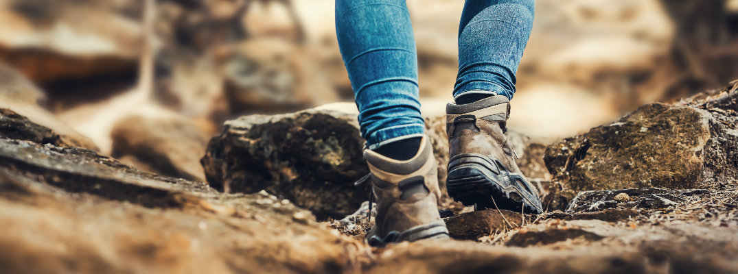 person in jeans and boots hiking over rocky terrain