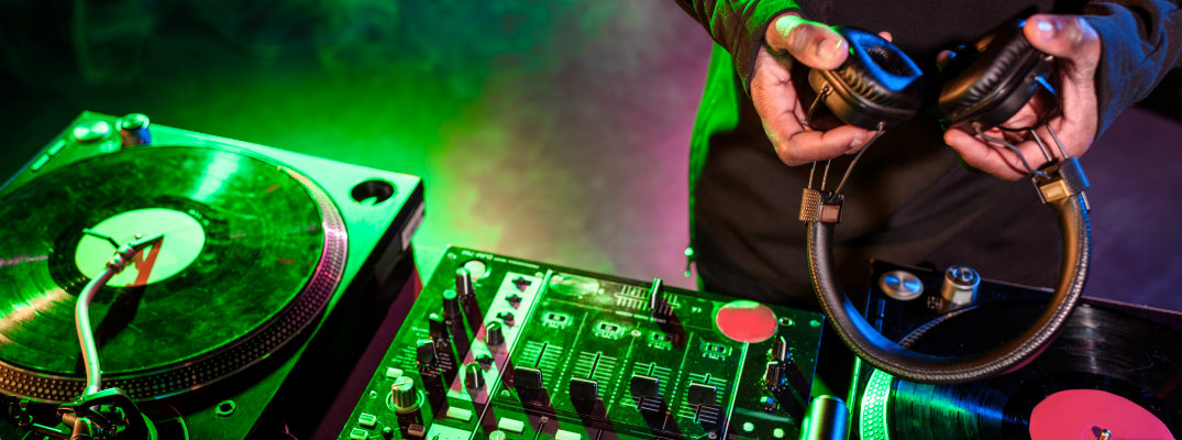 Dj holding headphones over mixing record board in a club with nightlife lighting and music