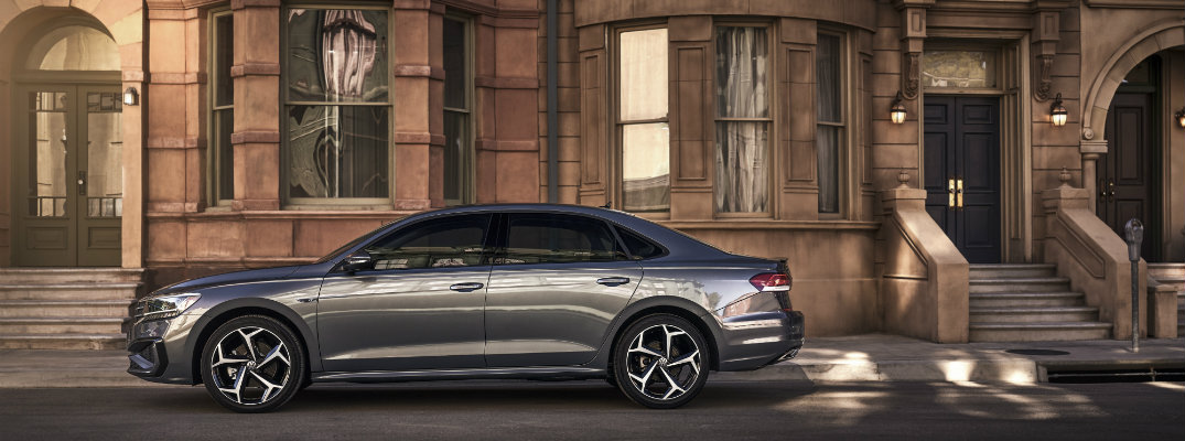 2020 Volkswagen Passat exterior side shot with dark gray metallic paint color parked outside an old fashioned brick and stone apartment building