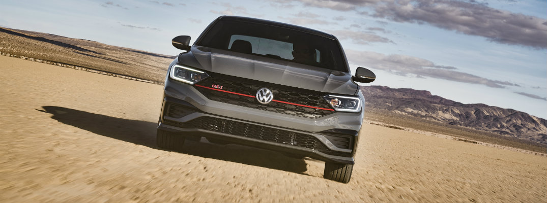 2019 Volkswagen Jetta GLI exterior front shot angled and showcasing red stripe on grille and GLI tag as it drives through a desert