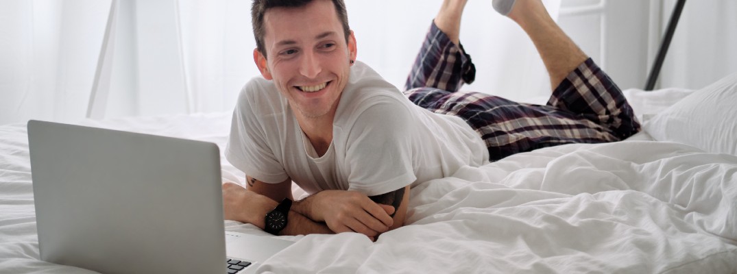 A stock photo of a person laying in bed using a laptop.