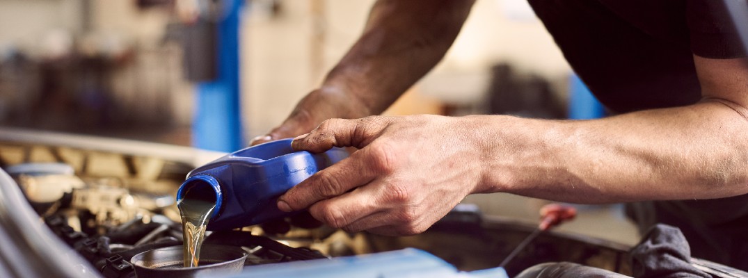 A stock photo of a person pouring oil into a car engine.