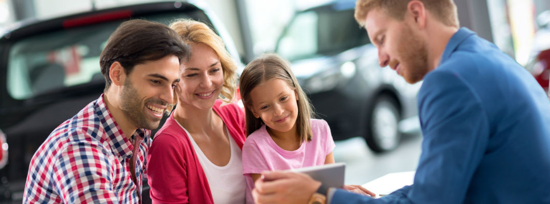 A stock photo of people looking at information in a car dealership.