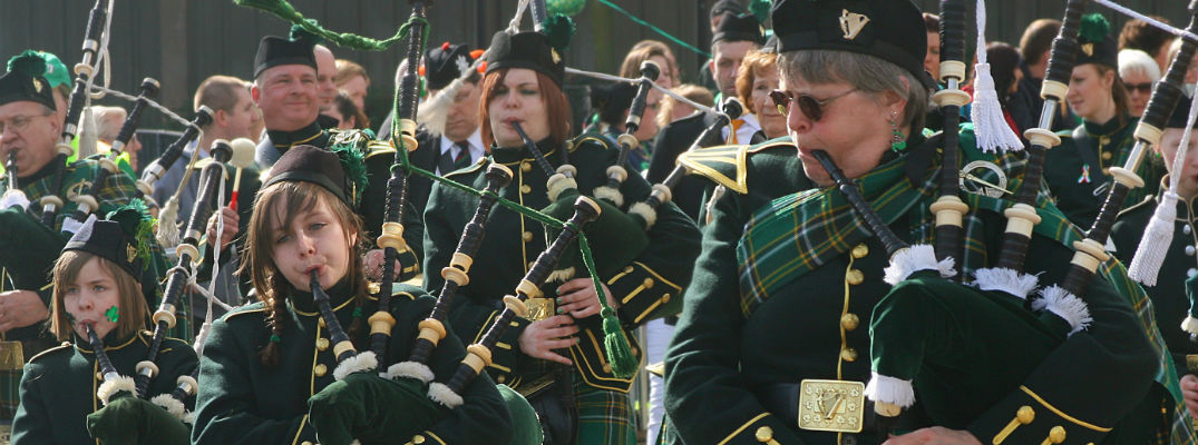 A stock photo of people playing bagpipes in a St. Patrick's Day parade.
