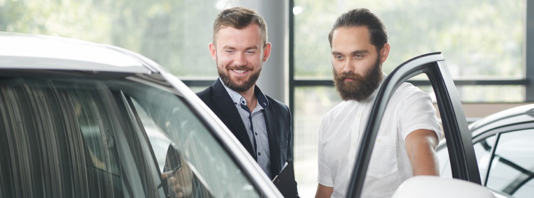 A stock photo of a person look at a vehicle with the help of a sales person.