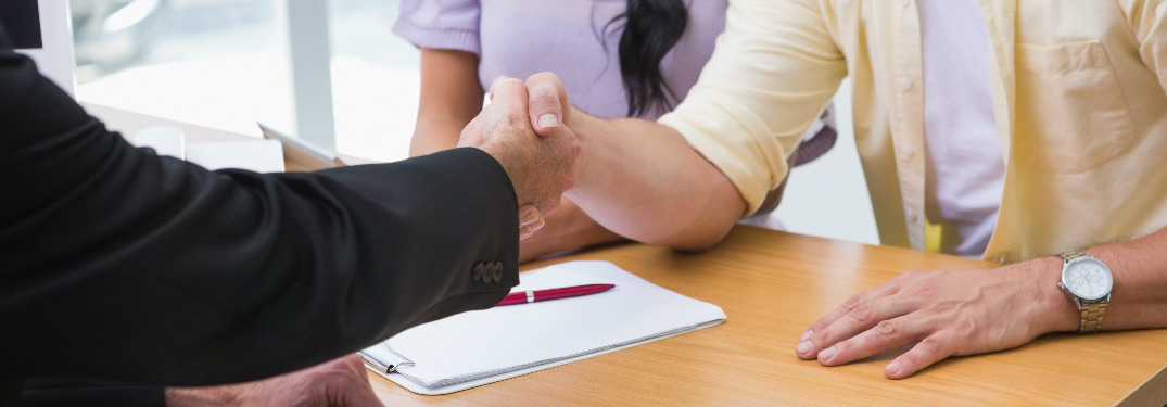 car salesman shaking hands with couple across desk