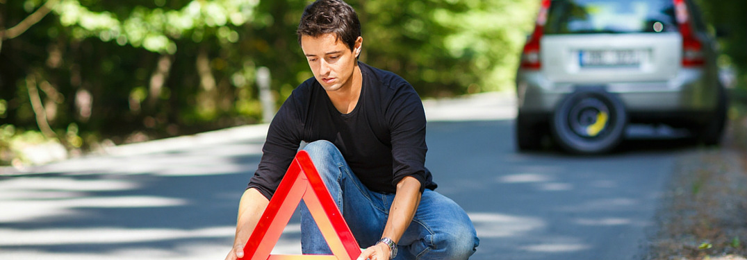 man setting up warning triangle near broken-down car
