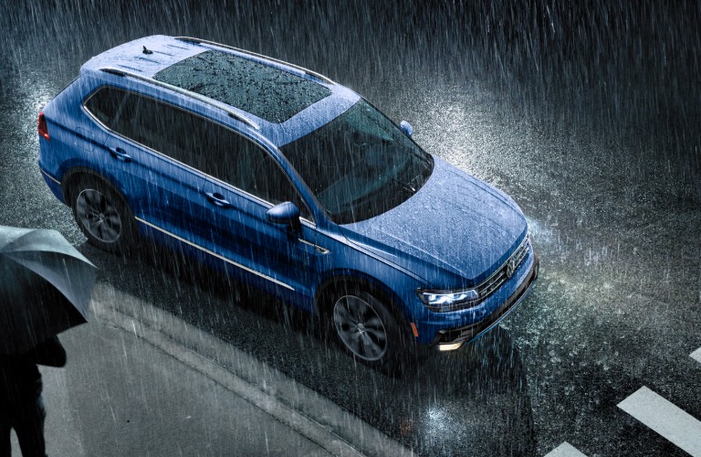 A blue 2020 Volkswagen Tiguan driving at night in the rain.