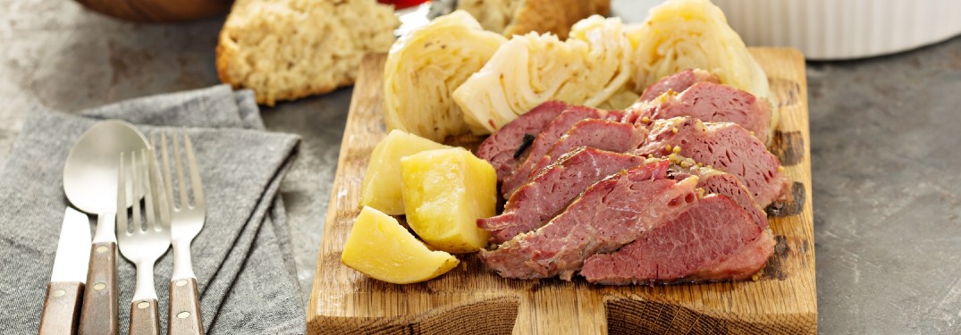 Corned beef and cabbage served on a wood board with silverware.