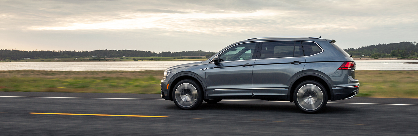 The side image of a gray 2020 Volkswagen Tiguan driving down an open coastal road.