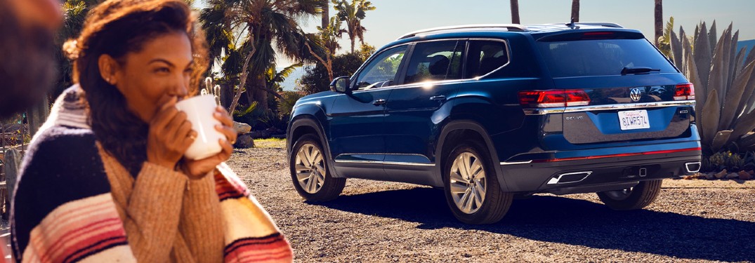A woman drinking from a cup next to a focused blue 2021 Volkswagen Atlas.